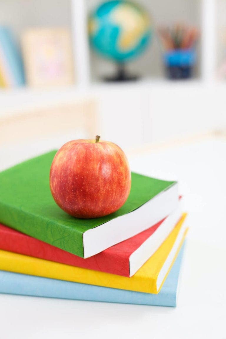 Three school books stacked with an apple on top in a classroom