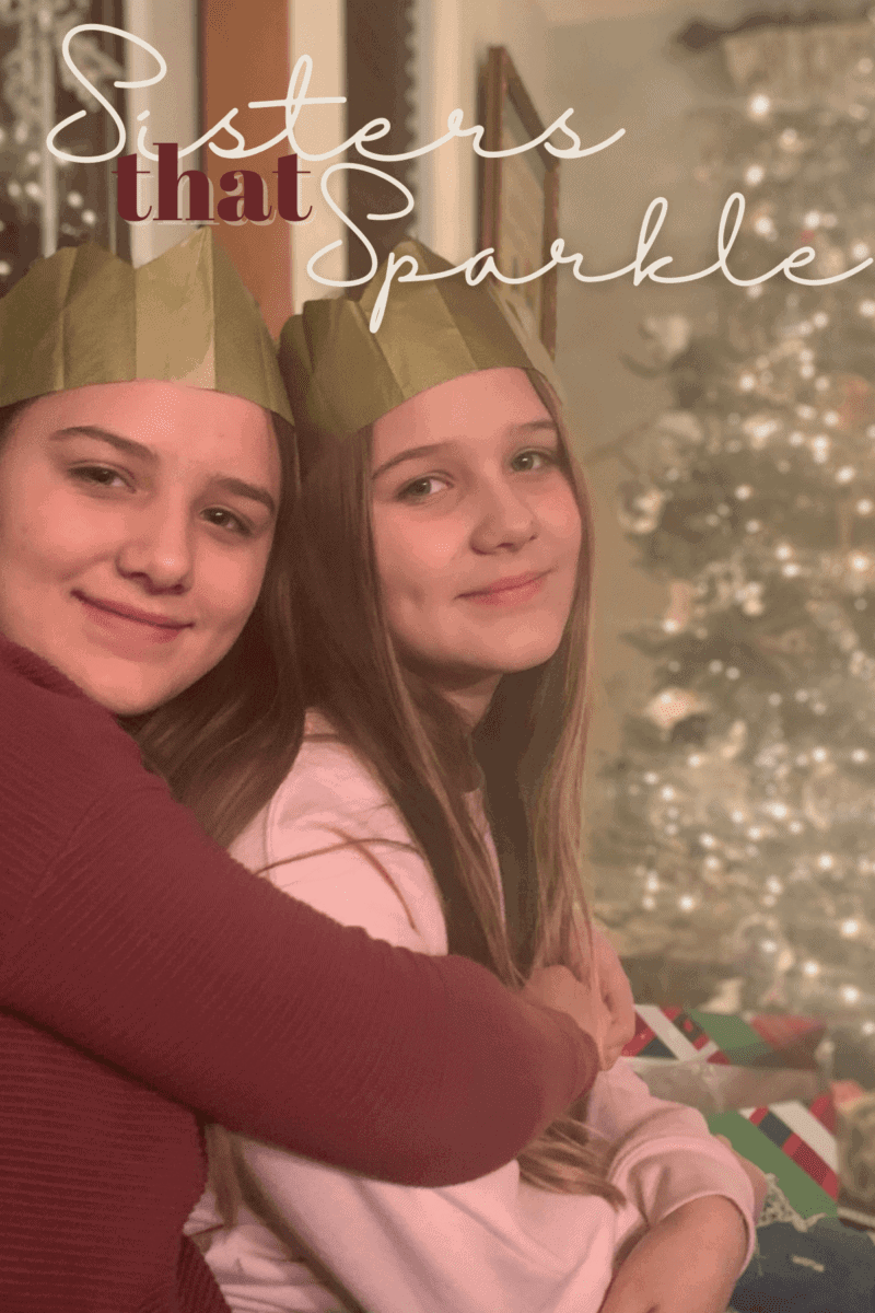 Two girls sitting in front of Christmas tree with white lights. 